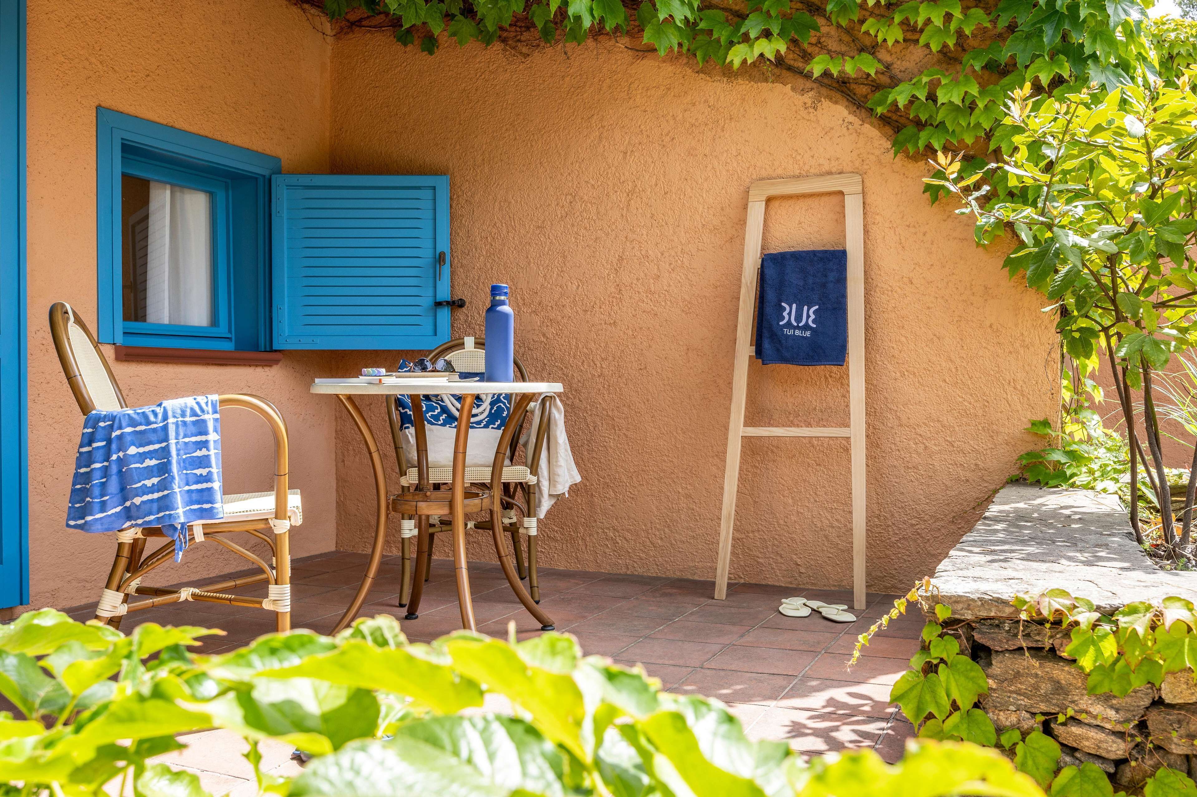 A small patio with a table and chairs, a blue towel, and a wooden ladder leaning against a wall.