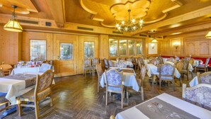 A restaurant with wooden walls and ceiling, tables with white tablecloths, and chairs with floral upholstery. - Hotel Restaurant Dragoner (Peiting)