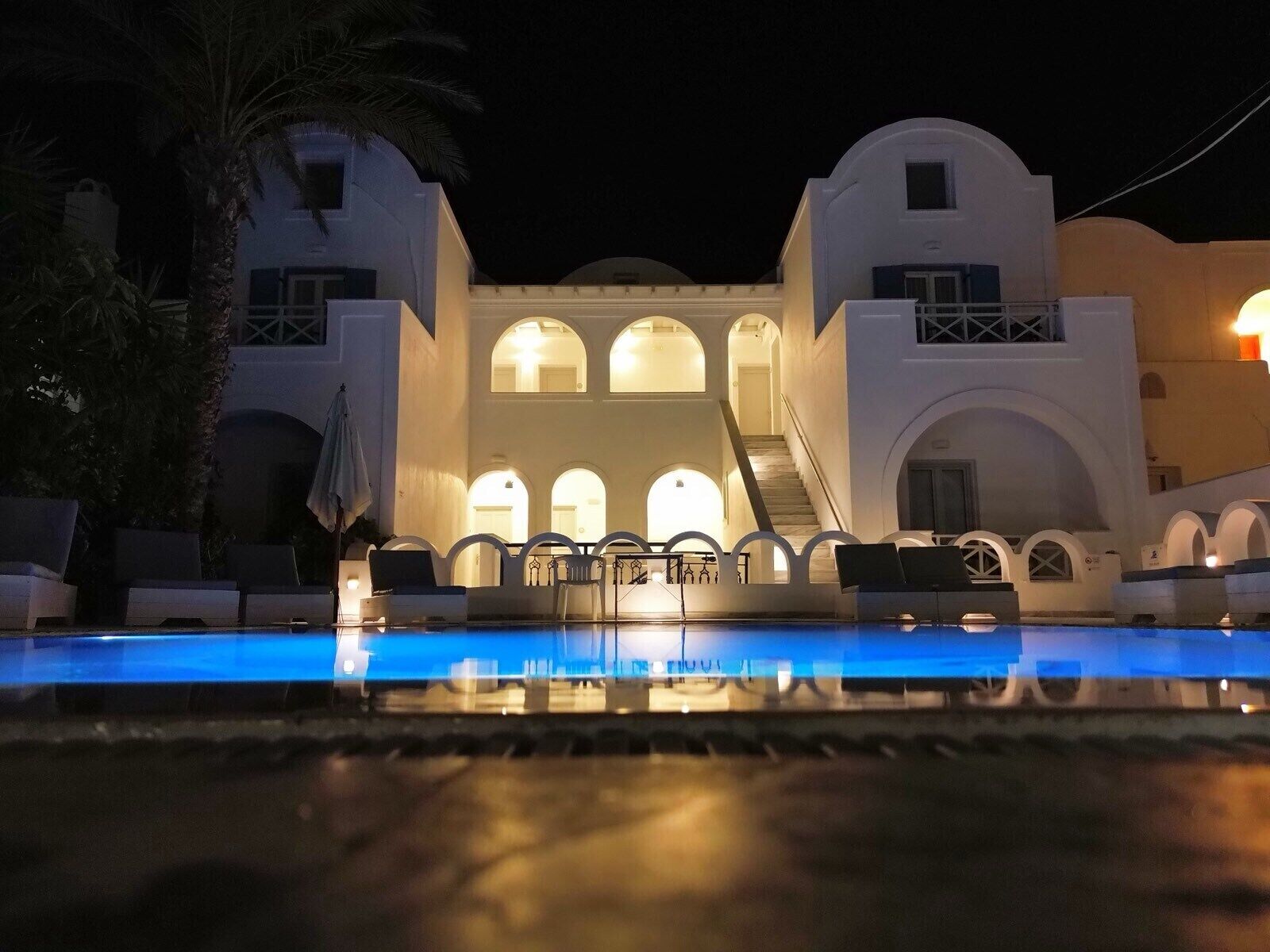 A hotel with a pool, arched balconies, and a staircase leading to the upper floors.