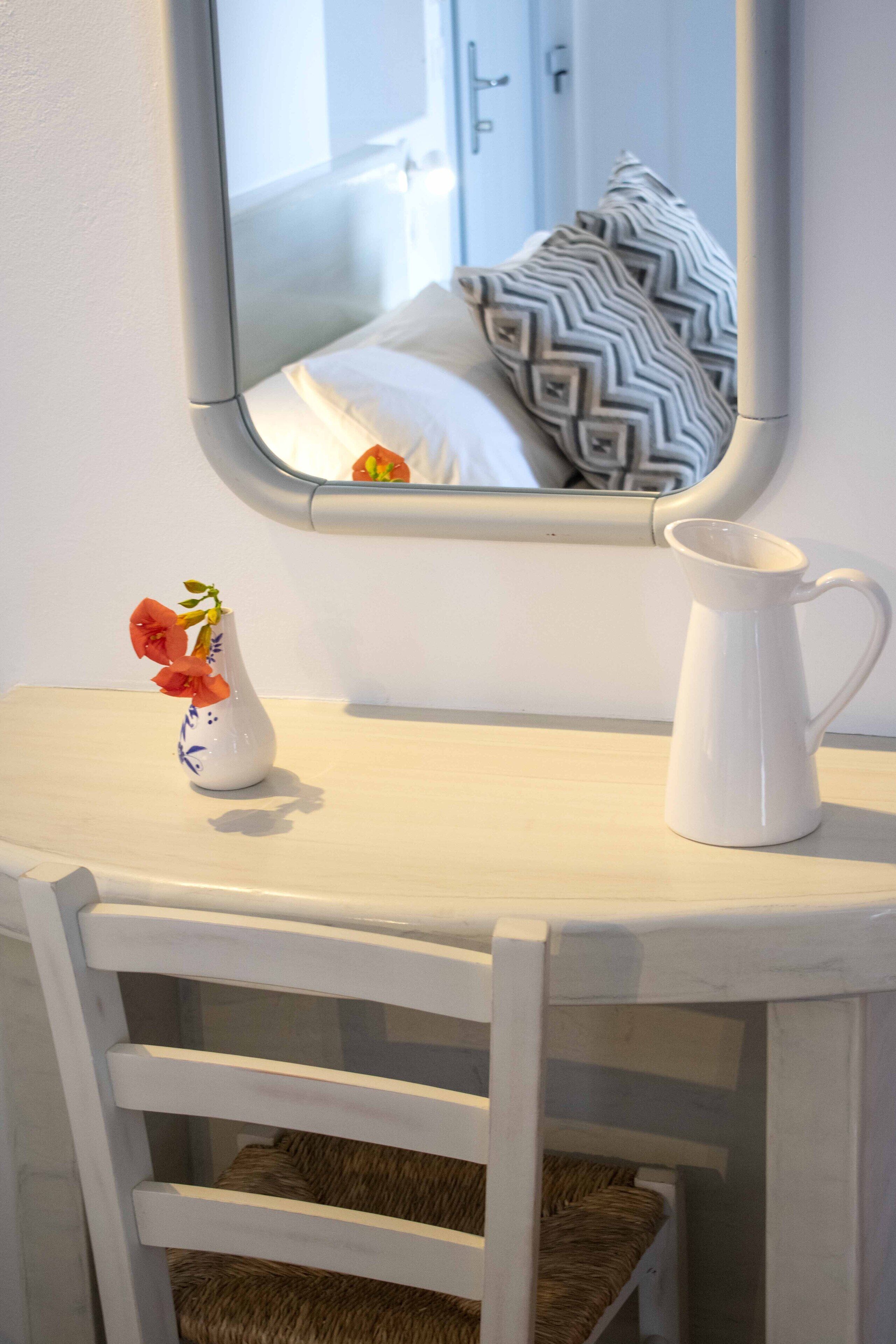 Une petite table blanche ornée d’un vase de fleurs et d’un pichet blanc.