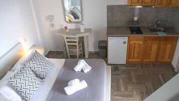 A compact hotel room with a bed, a small desk, a mirror, a kitchenette, and a bathroom.