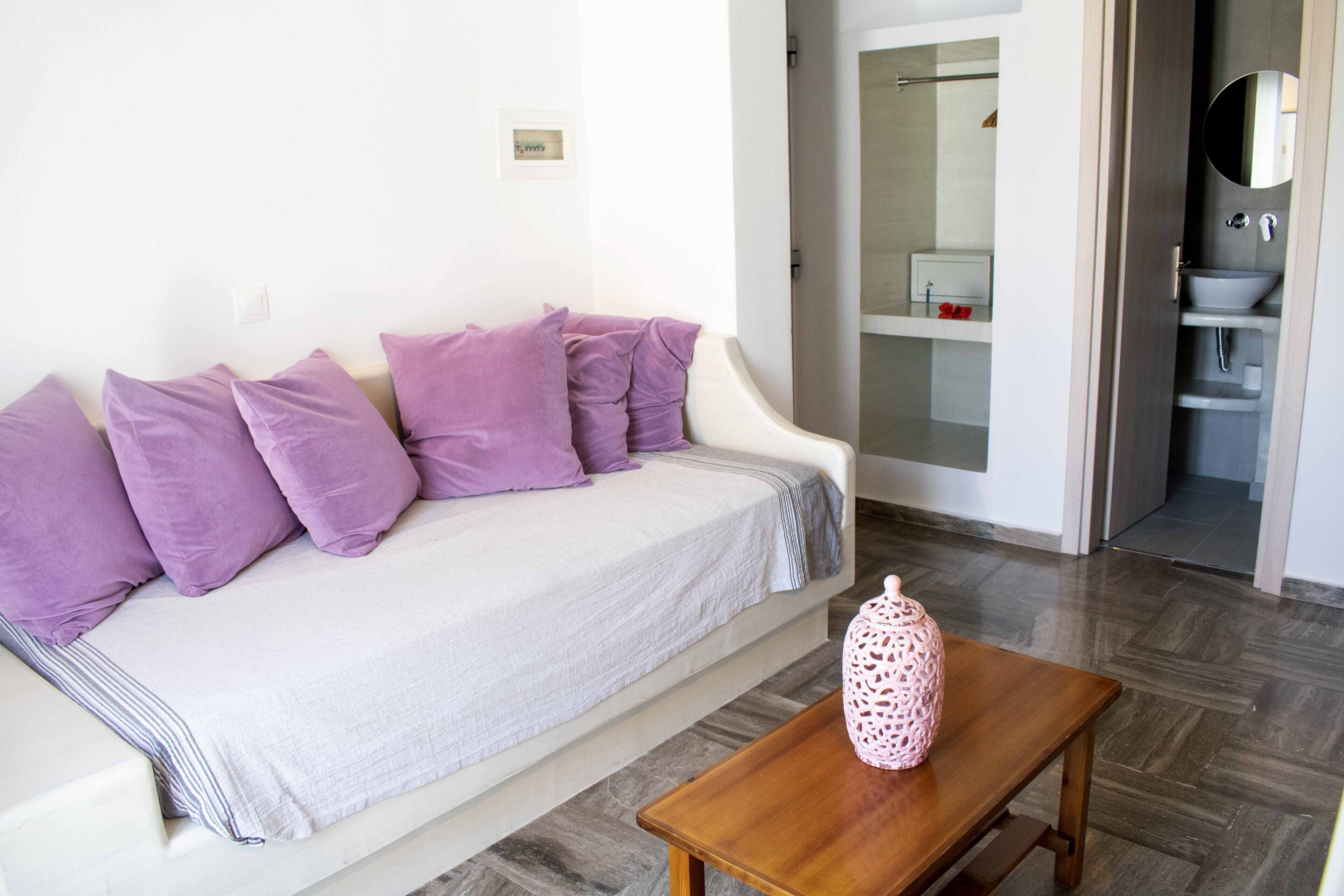 Un salon moderne avec un canapé blanc, des coussins violets et une table basse en bois sur laquelle est posé un vase décoratif.