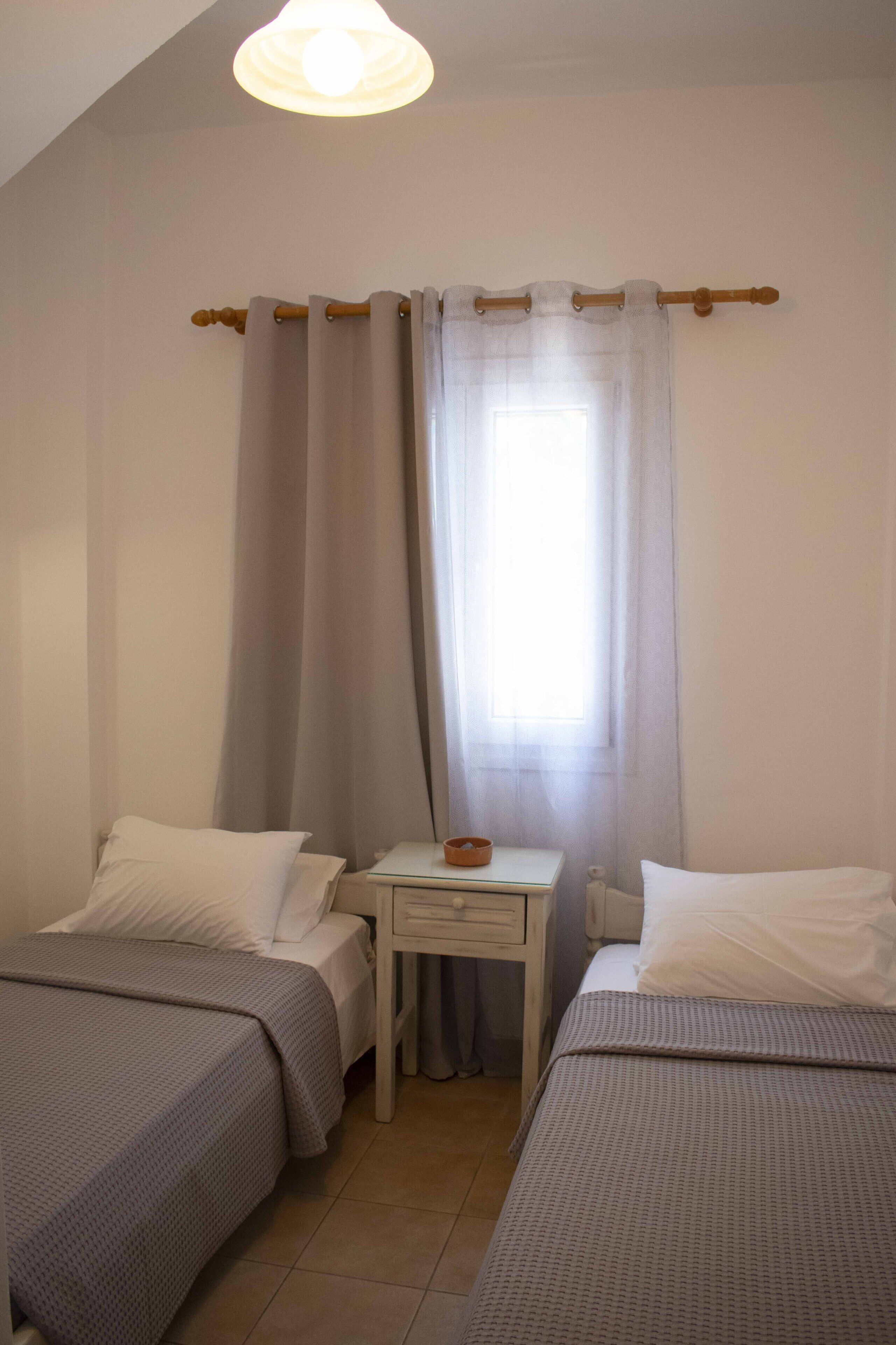 Een slaapkamer met twee bedden, een klein tafeltje en een raam met gordijnen.