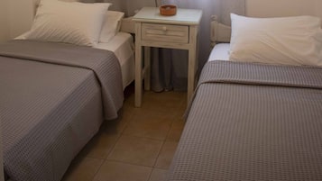 Een slaapkamer met twee bedden, een klein tafeltje en een raam met gordijnen.