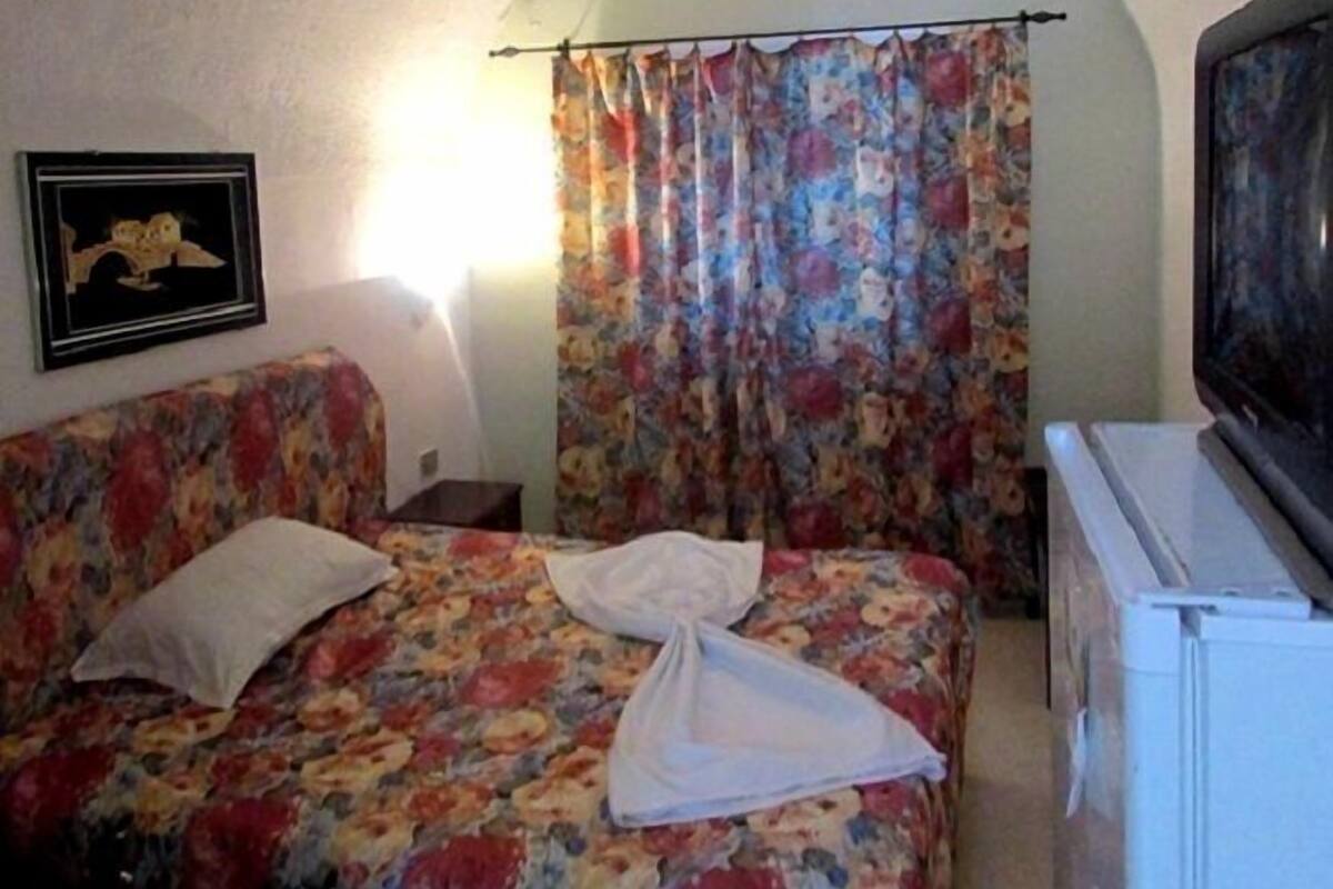 Una habitación con cama, televisión, un cuadro en la pared y cortina.