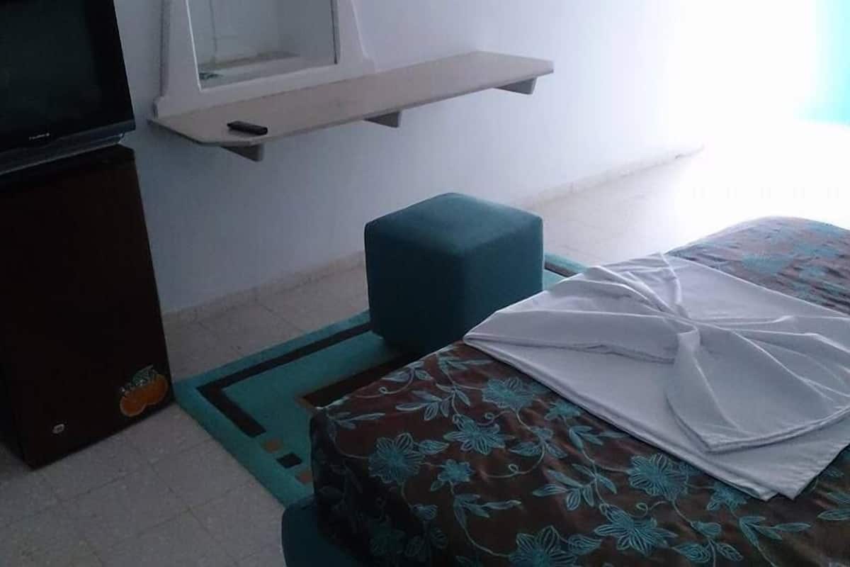 Una habitación pequeña con una cama, un televisor y una ventana.