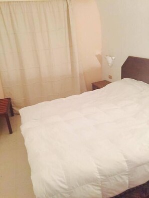A hotel room with a bed, a nightstand, a chair, and a curtain. - Hôtel Solymar Beach (Soliman)