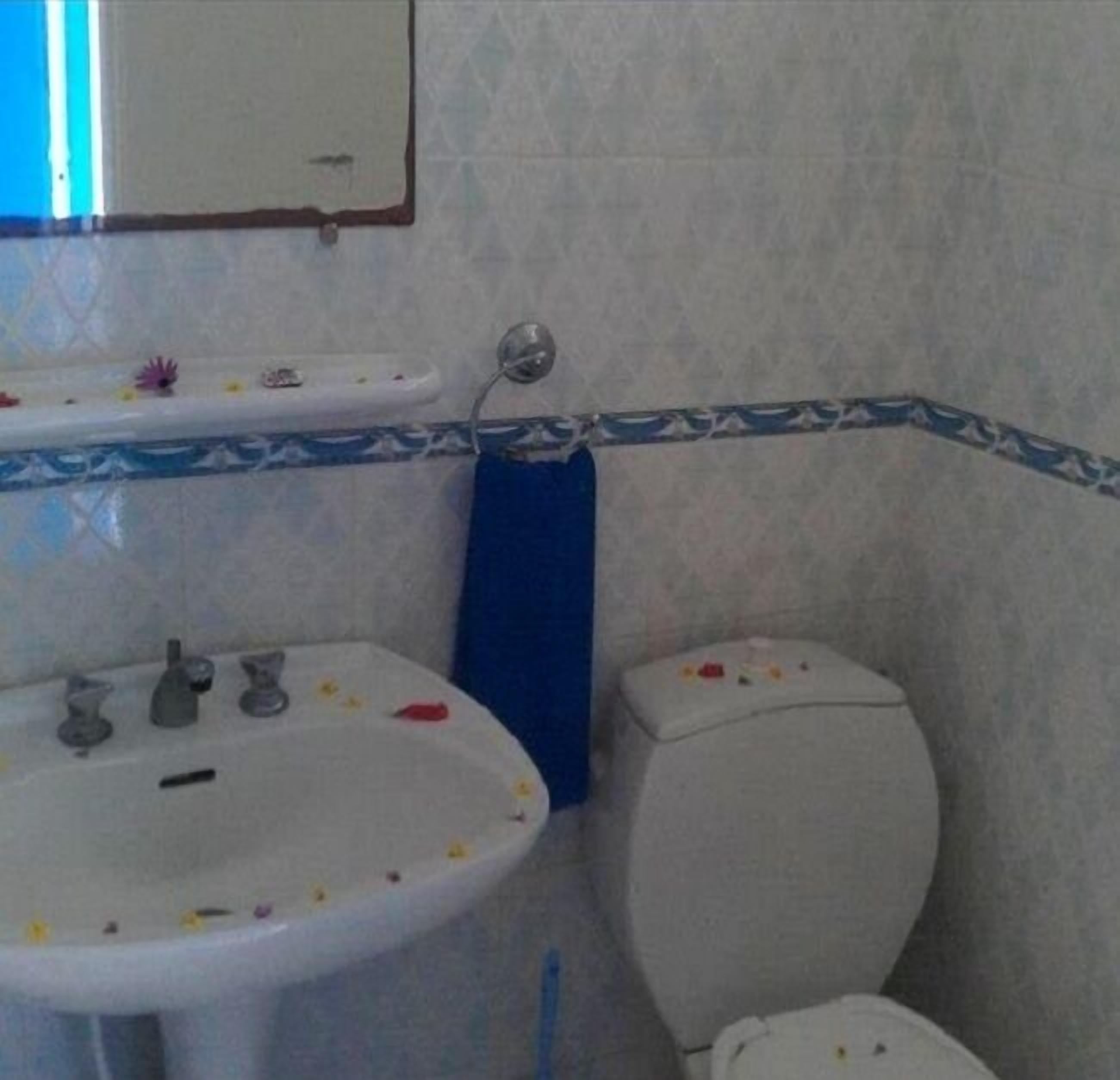 A bathroom with a white sink, mirror, and toilet. There is a blue towel hanging on the wall.