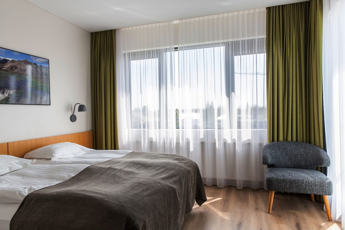 Habitación de hotel con dos camas, una silla, un cuadro y cortinas traslúcidas.