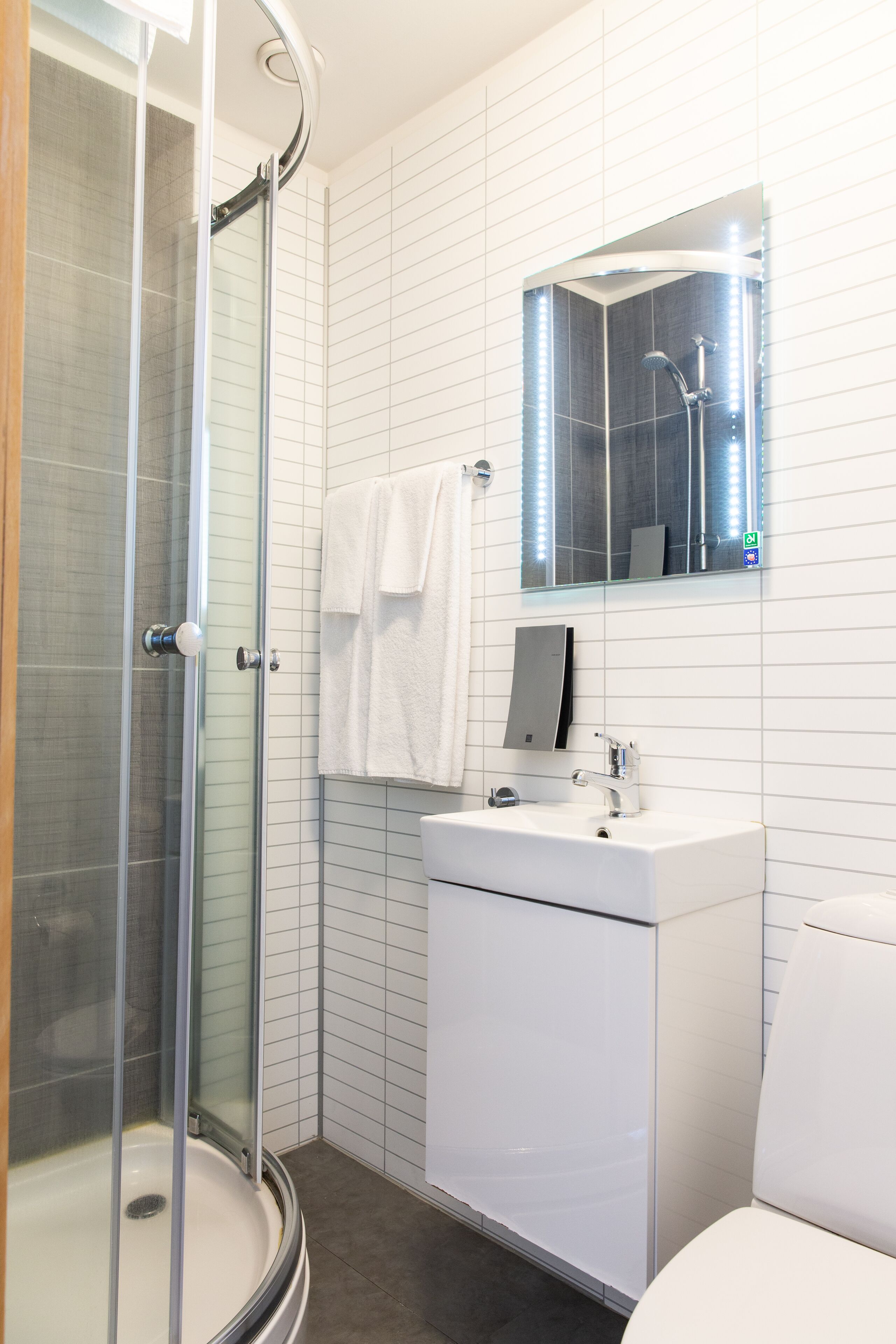 Un baño moderno con ducha de vidrio, lavamanos blanco y espejo superior.