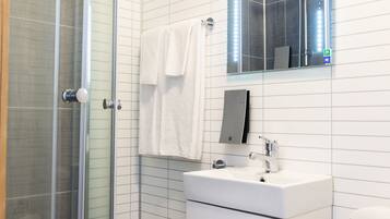 Un baño moderno con ducha de vidrio, lavamanos blanco y espejo superior.
