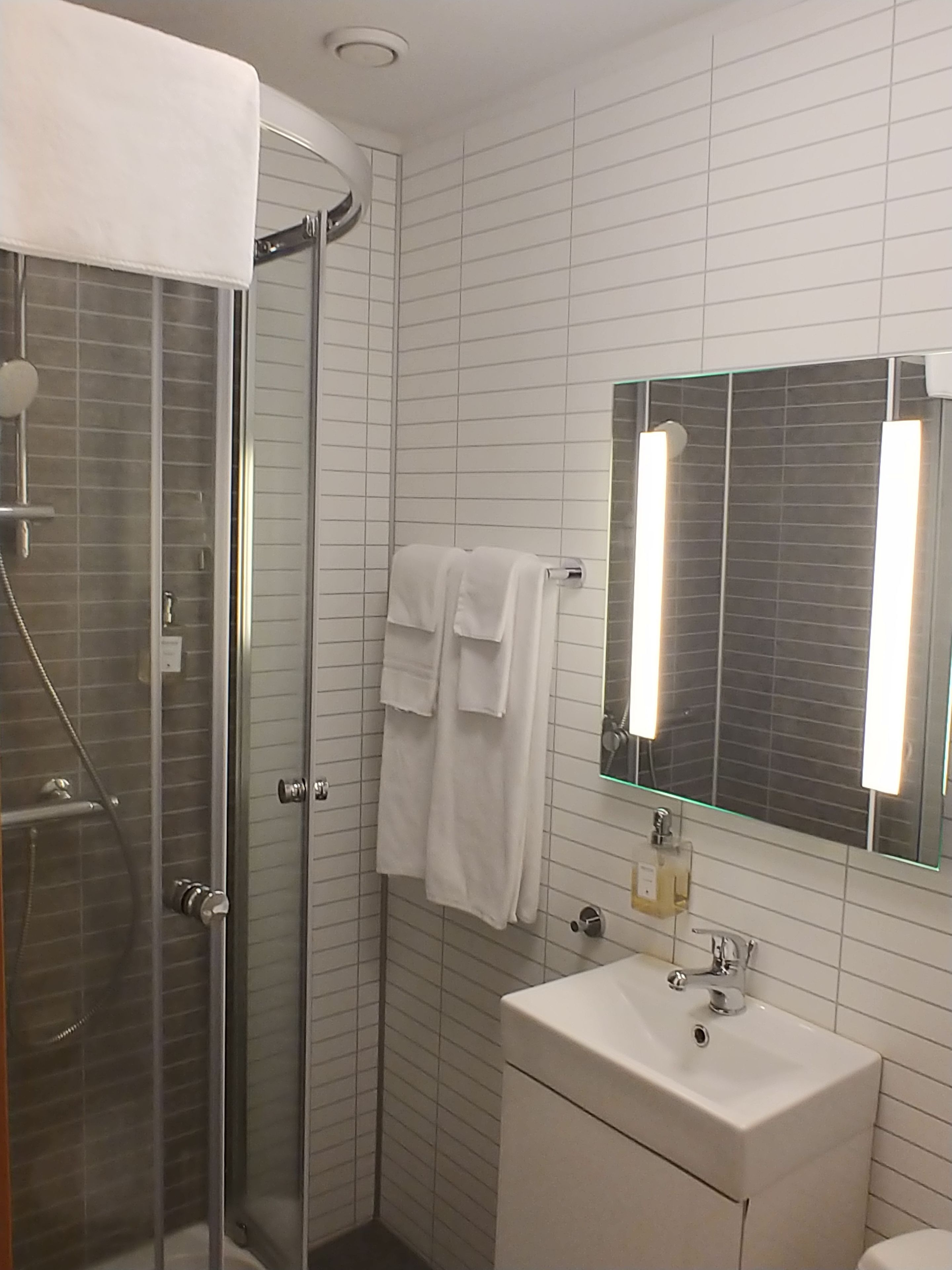 A modern bathroom with a glass shower enclosure, a white sink with a mirror above it, and a towel rack with two towels.