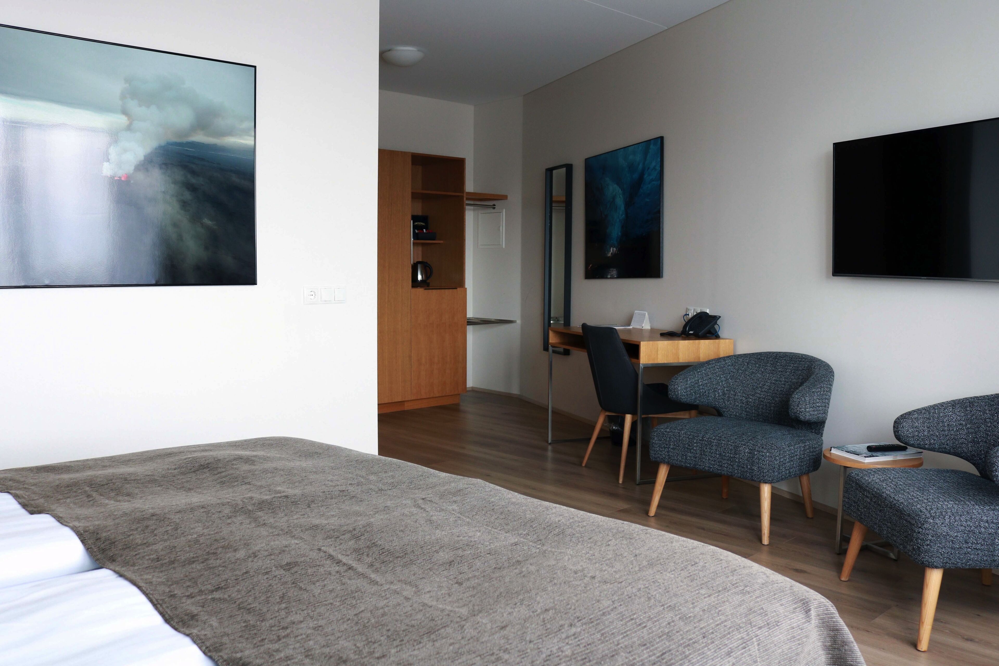 A modern hotel room with a large bed, a desk with a chair, a TV, and artwork on the walls.