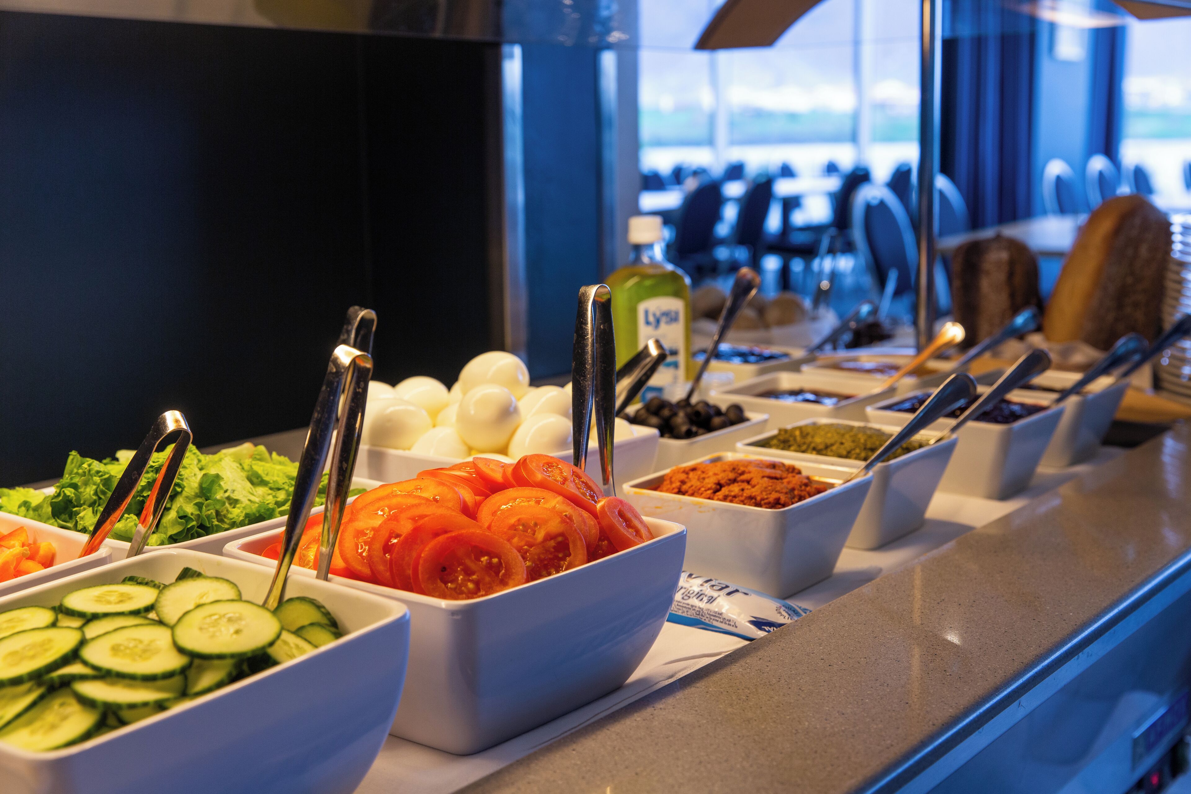 A buffet with various food options including cucumbers, tomatoes, olives, and eggs.