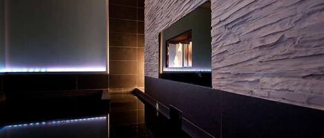 A modern spa area with a stone-textured wall, a large mirror, and a sleek black floor.