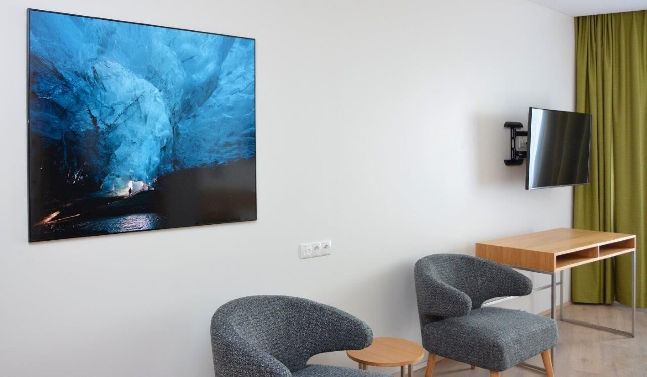 Una habitación con un cuadro grande de una cueva azul, un televisor de pantalla plana, dos sillones grises, una mesita de madera y una cortina verde.