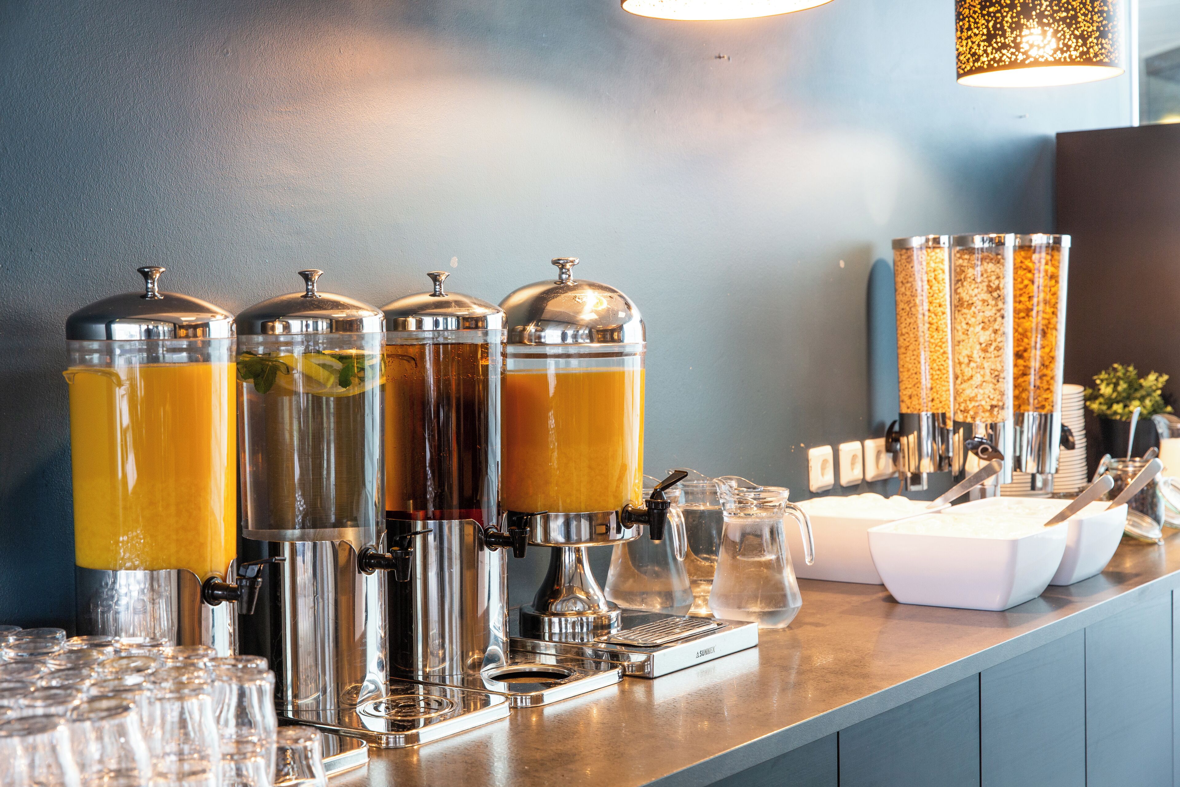 A bar area with multiple beverage dispensers, glasses, and a coffee machine.
