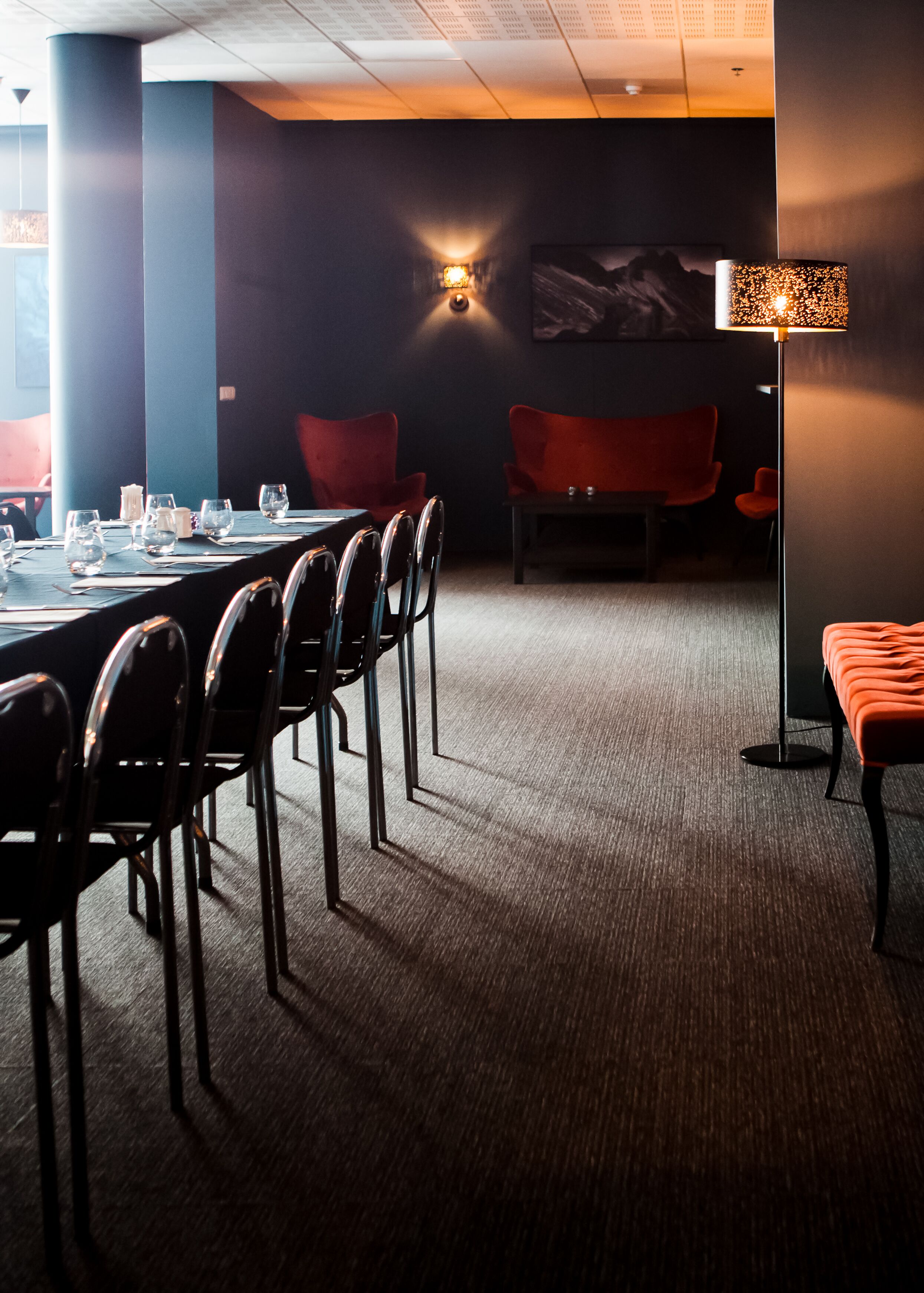 A conference room with a long table, chairs, a standing lamp, and a painting on the wall.