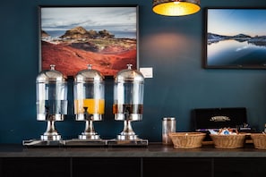 A bar area with three beverage dispensers, two framed landscape pictures, and a basket of snacks. - Hotel Selfoss (Selfoss)
