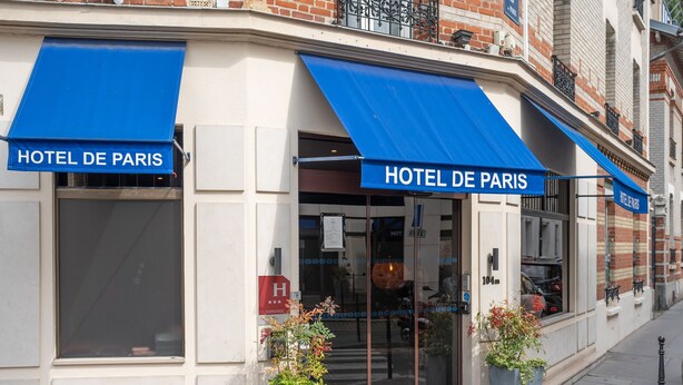 The exterior of Hotel De Paris with blue awnings, large windows, and potted plants at the entrance. - Hotel de Paris (Boulogne-Billancourt)