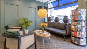 A lobby with a sofa, chairs, a coffee table, a potted plant, a hanging light fixture, and a magazine rack. - Hotel de Paris (Boulogne-Billancourt)