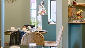 A dining area with a table set for two, a decorative wall piece, and a kitchen area with a fruit display. - Hotel de Paris (Boulogne-Billancourt)