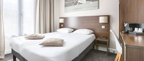 A hotel room with a large bed, a desk, a chair, a nightstand, and a wall-mounted TV.