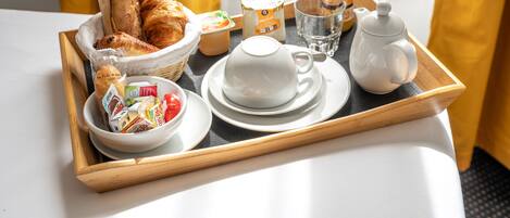 A breakfast tray with croissants, yogurt, juice, and a teapot on a table.