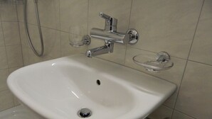 A bathroom with a white sink, a glass soap dish, and a handheld showerhead. - Swiss Star Delsbergerallee (Basel)
