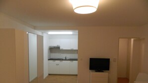 A compact kitchen with white cabinets, a black TV on a stand, and a wooden floor. - Swiss Star Delsbergerallee (Basel)