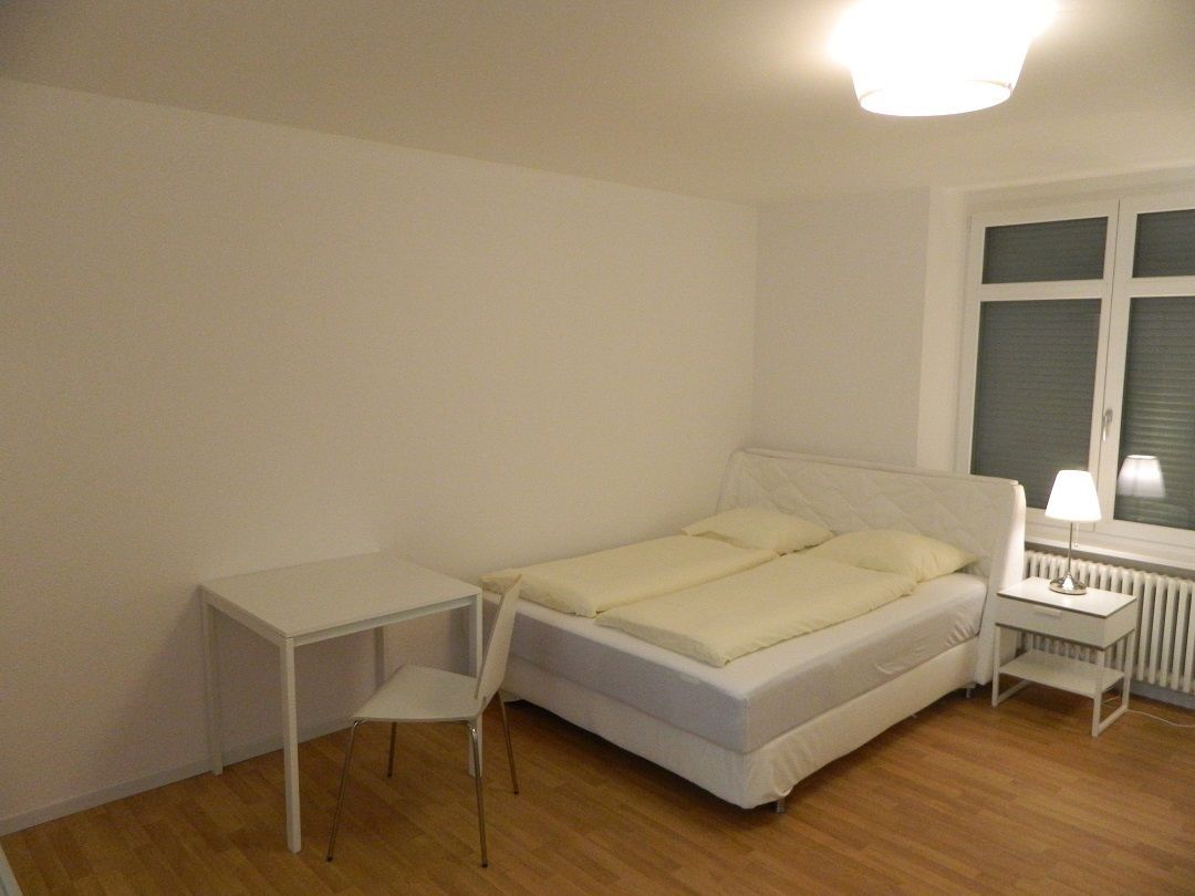 Ein Schlafzimmer mit einem Bett, einem kleinen Tisch, einem Stuhl und einer Lampe.