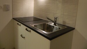 A compact kitchen with a stainless steel sink, black countertop, and white tiled walls. - Swiss Star Delsbergerallee (Basel)