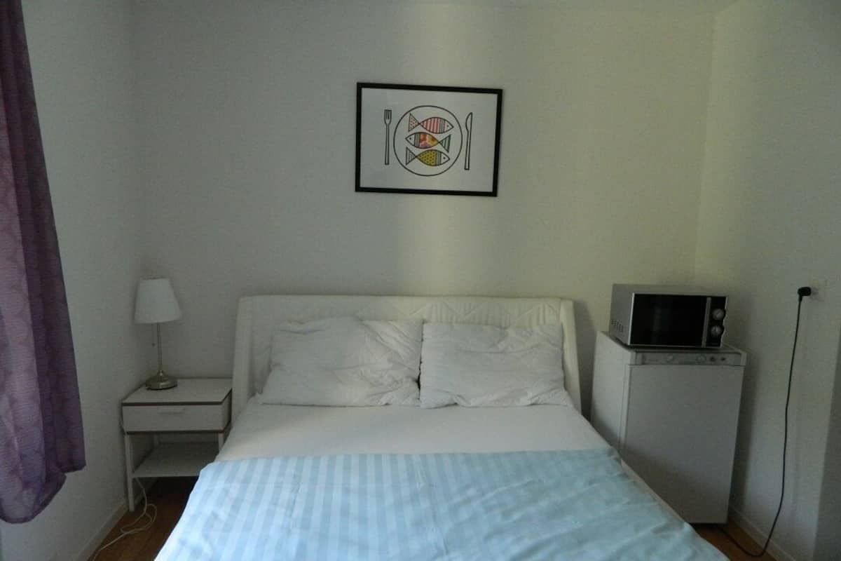 Un dormitorio con cama, mesita de noche, televisor y un cuadro colgado en la pared.