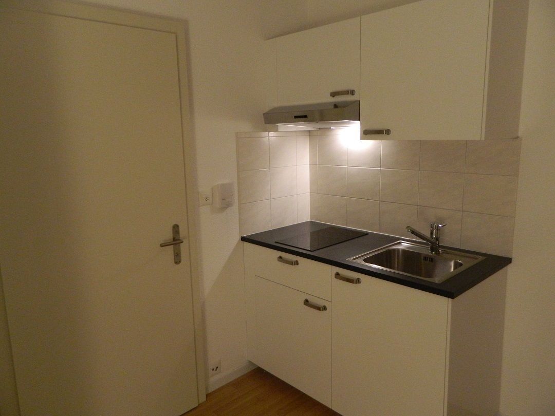 A small kitchen with white cabinets, a black countertop, and a stainless steel sink.