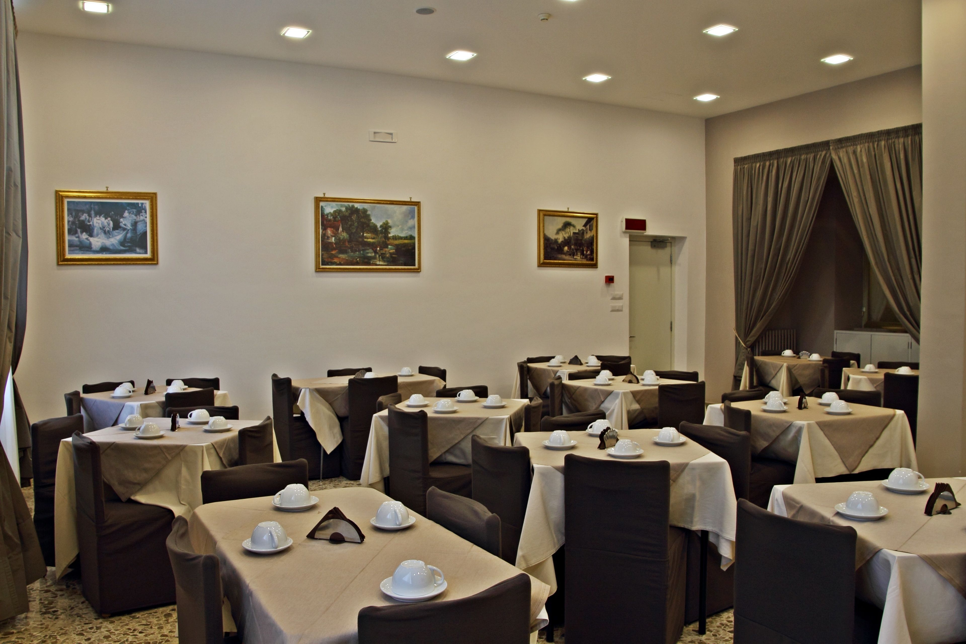 En hotellrestaurang med flera bord, där varje bord är dukat med vita dukar och vitt porslin.
