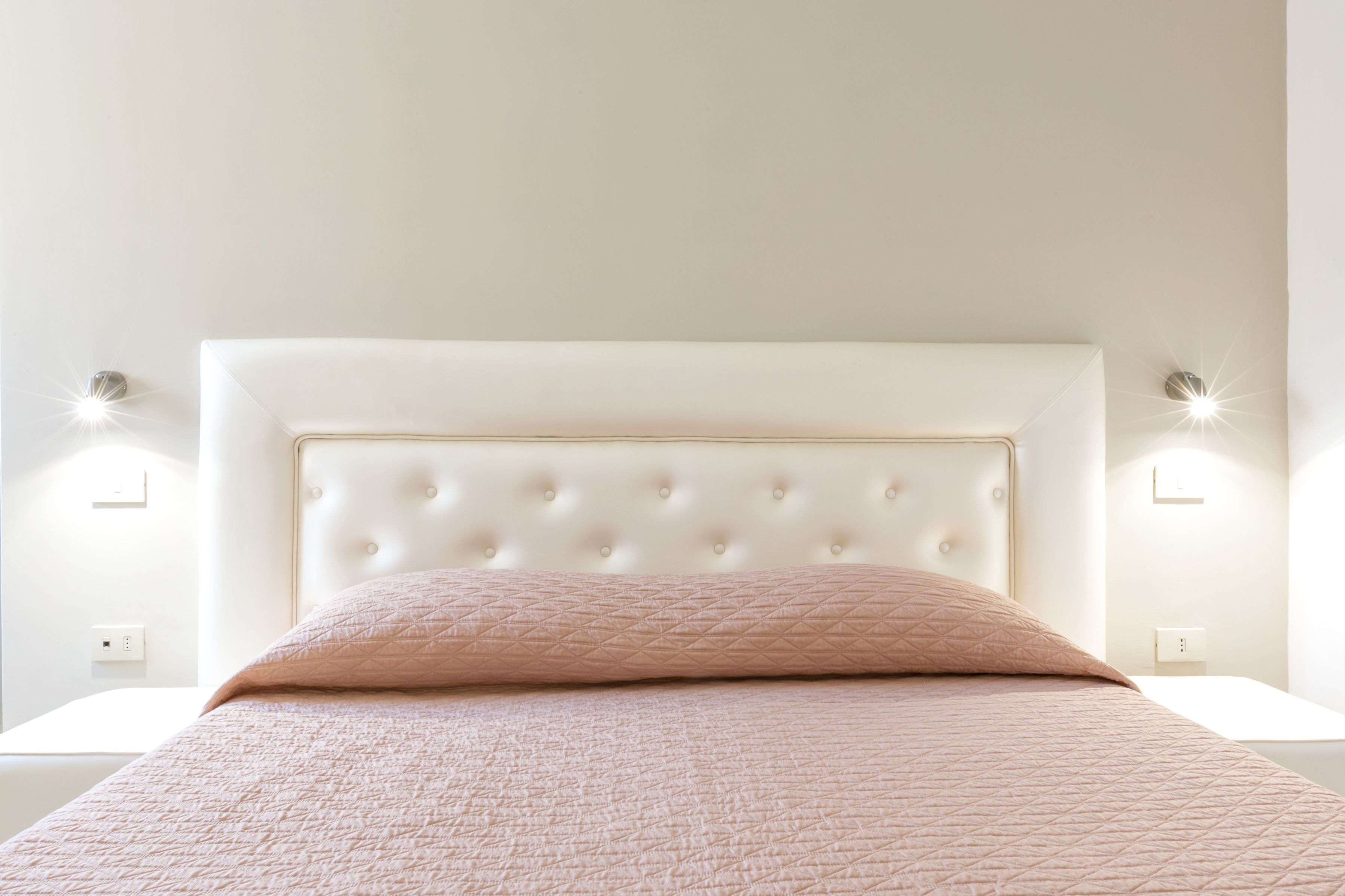 A bed with a tufted headboard, a pink quilted bedspread, and two bedside lamps on white nightstands.