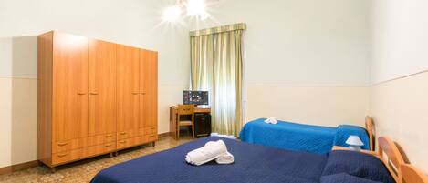 Een hotelkamer met een grote kast, een bureau, twee bedden met blauw beddengoed en een raam met gordijnen.