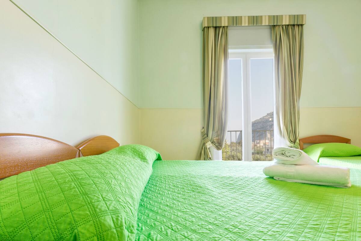 Ein Hotelzimmer mit Bett, Fenster mit Vorhängen und Blick auf ein Gebäude.