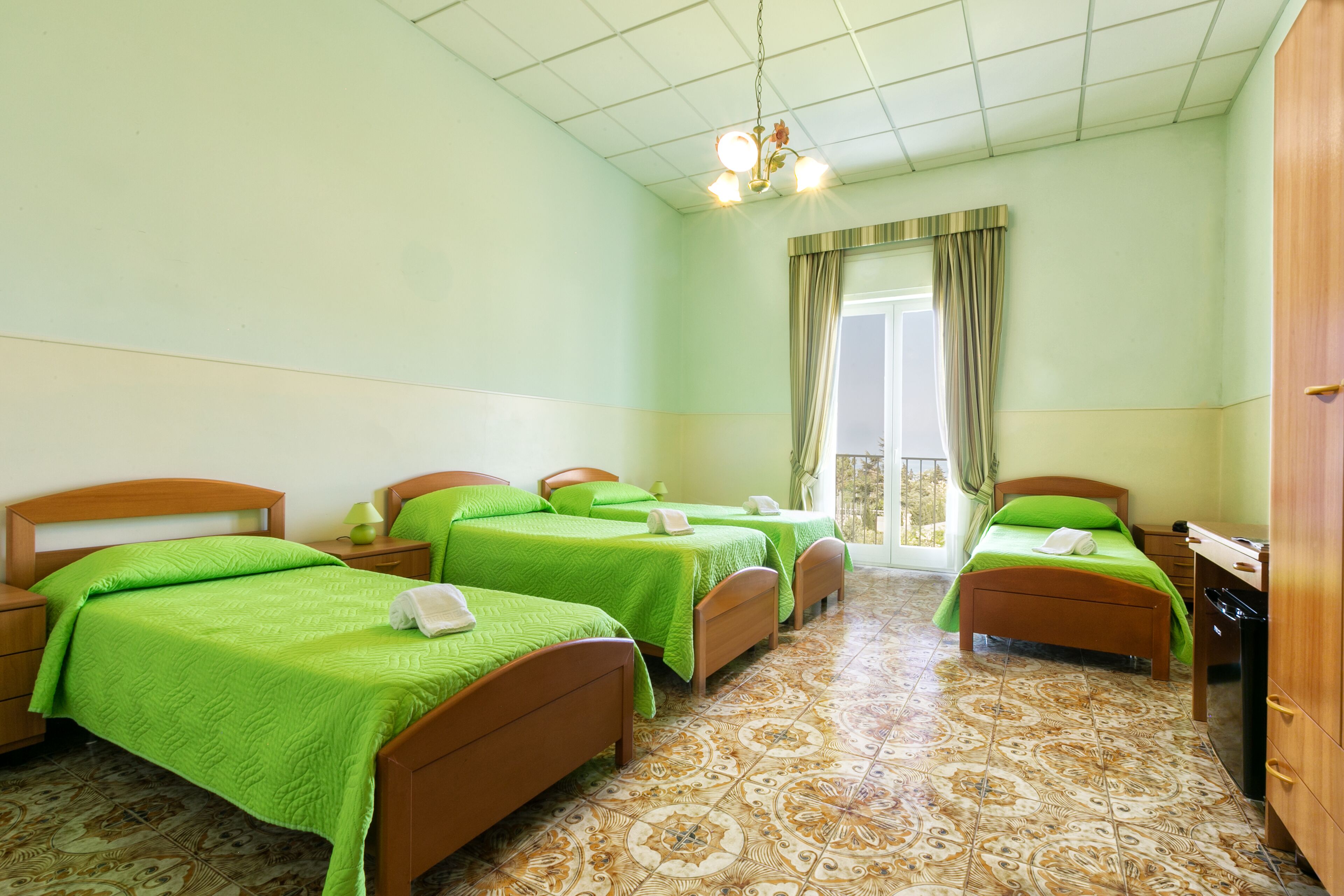A hotel room with three beds, a wooden wardrobe, a tiled floor, and a window with curtains.