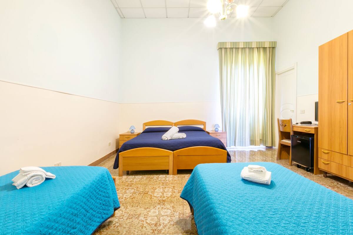 Ein Hotelzimmer mit zwei Einzelbetten, einem Schreibtisch, einem Kleiderschrank und einem Badezimmer.