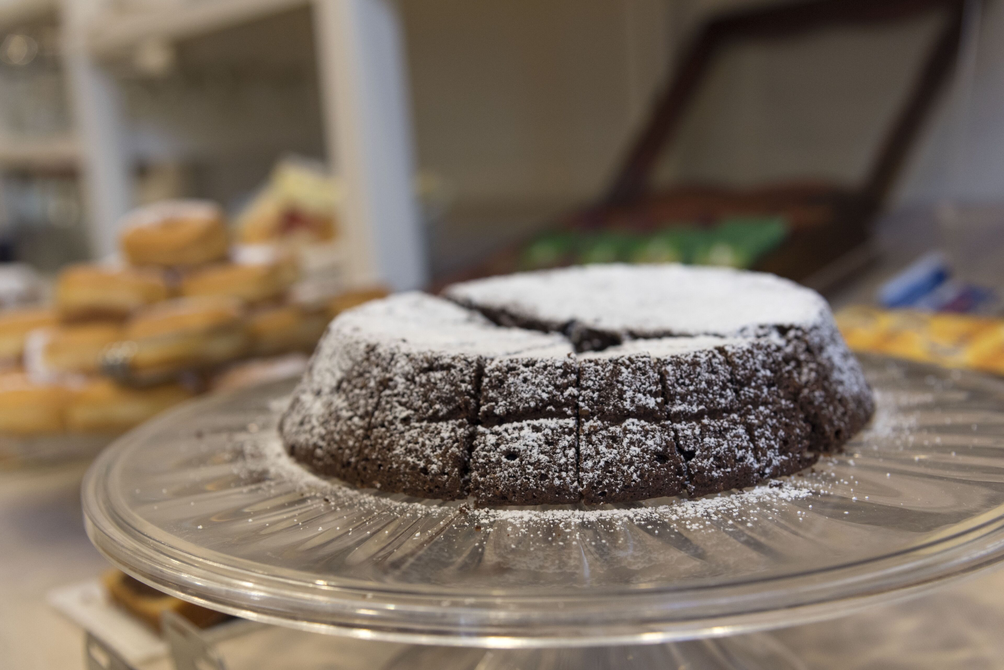 A chocolate cake on a glass plate with powdered sugar on top.