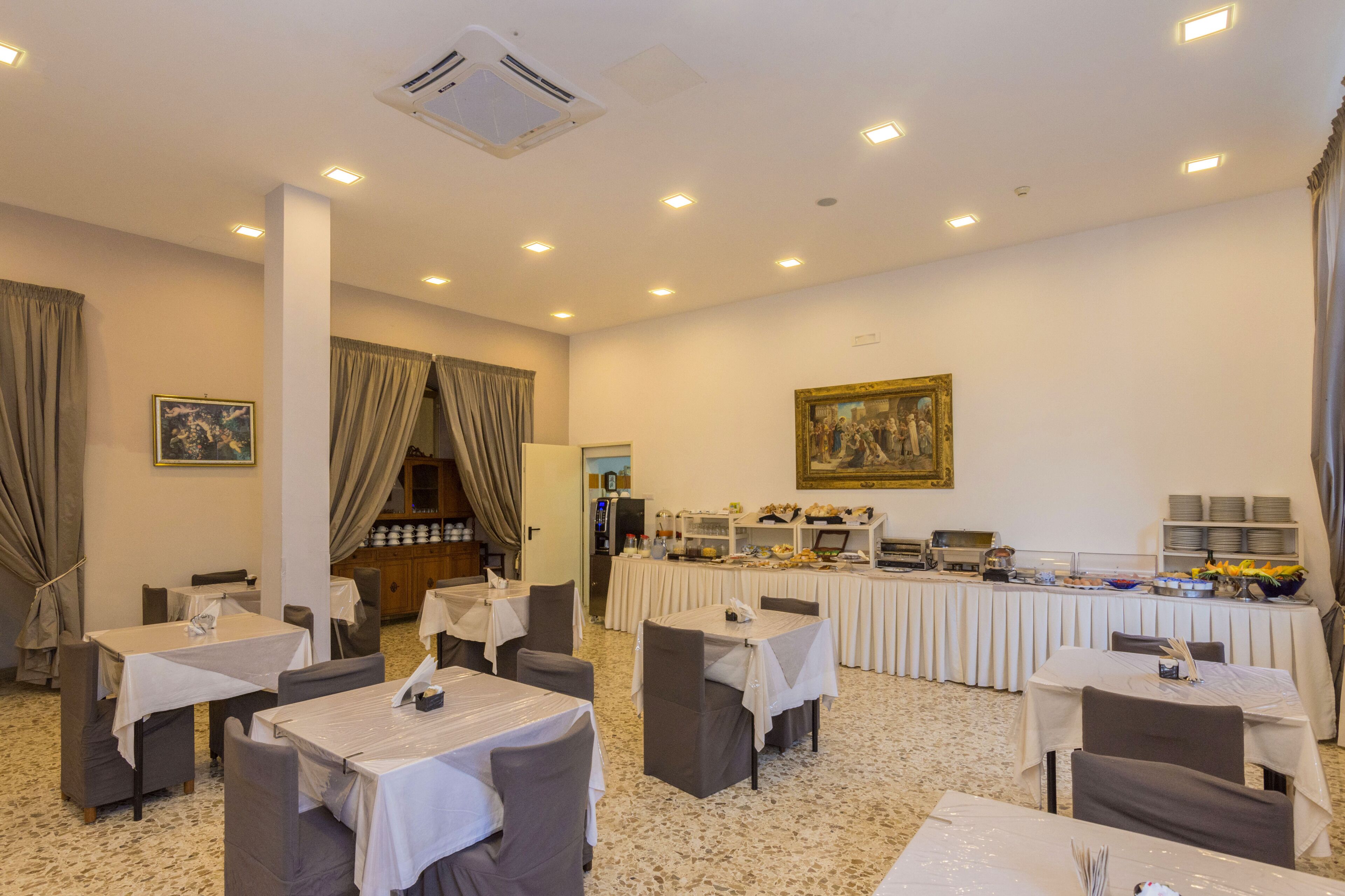 Une salle à manger d’hôtel avec des tables, des chaises, un buffet et un tableau accroché au mur.