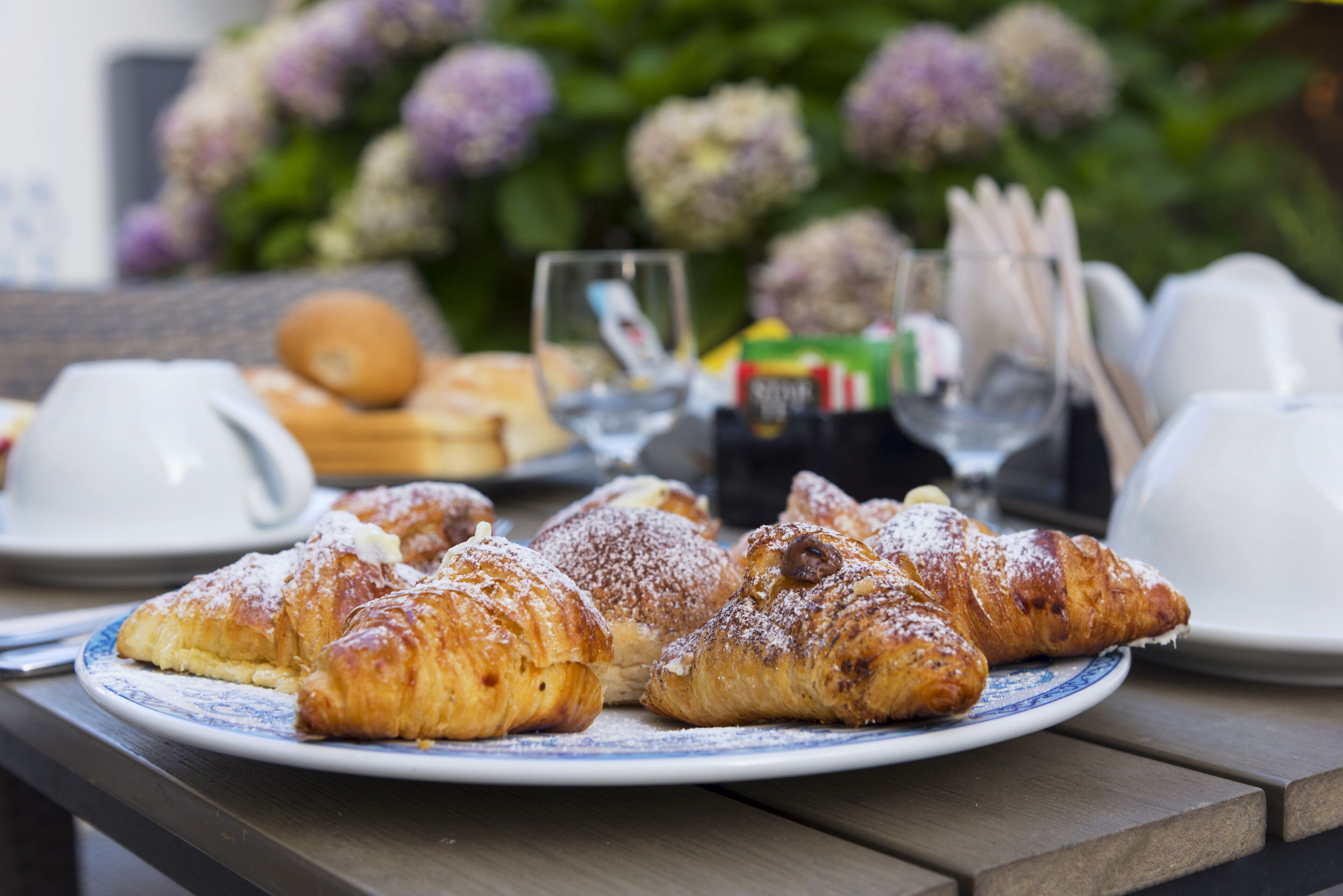 A table with pastries and a coffee cup, set outdoors with flowers in the background.