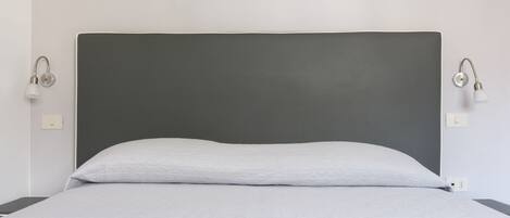 A bed with a grey headboard, white bedding, and two wall-mounted light fixtures.