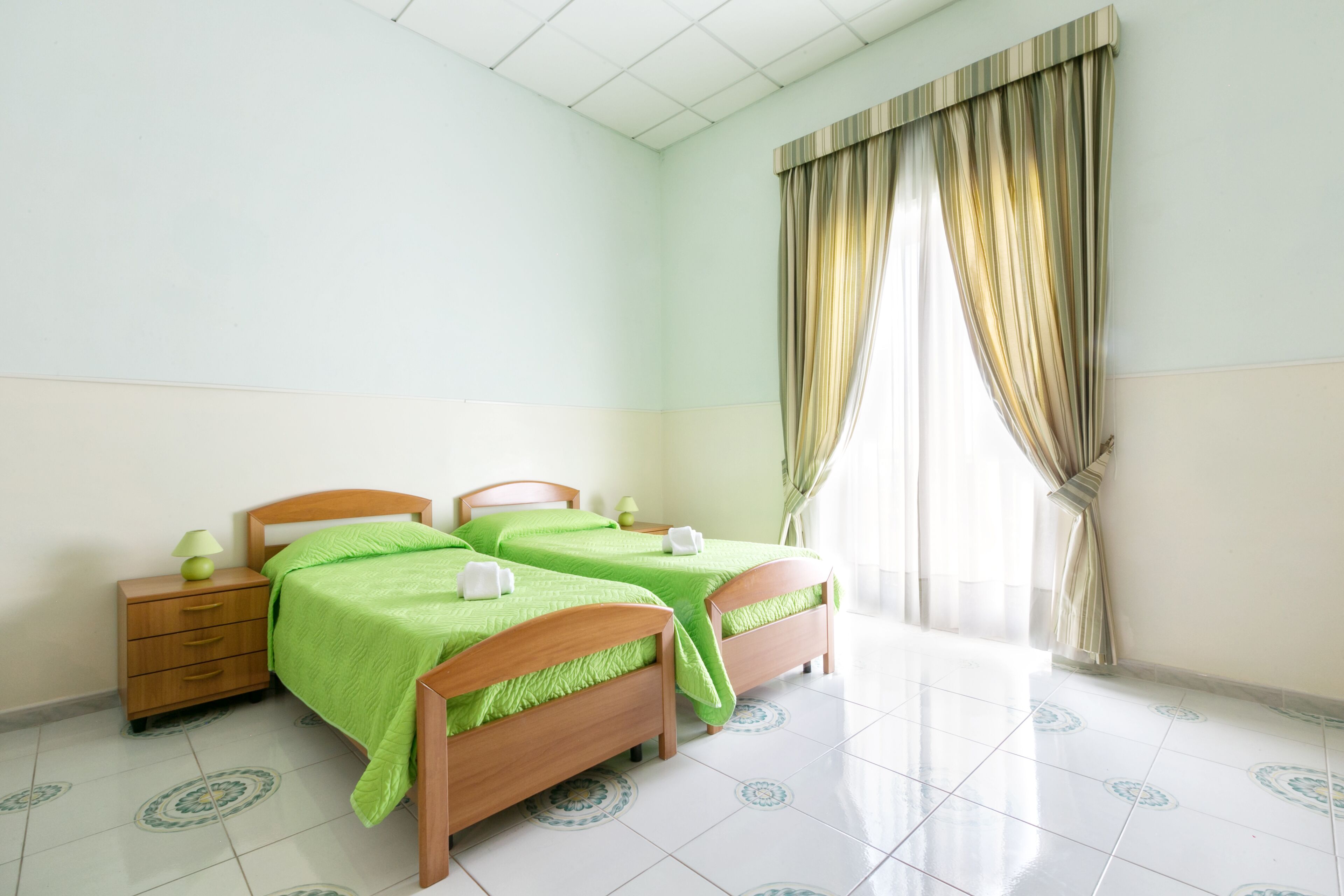 A room with two beds, a nightstand, and a window with curtains.