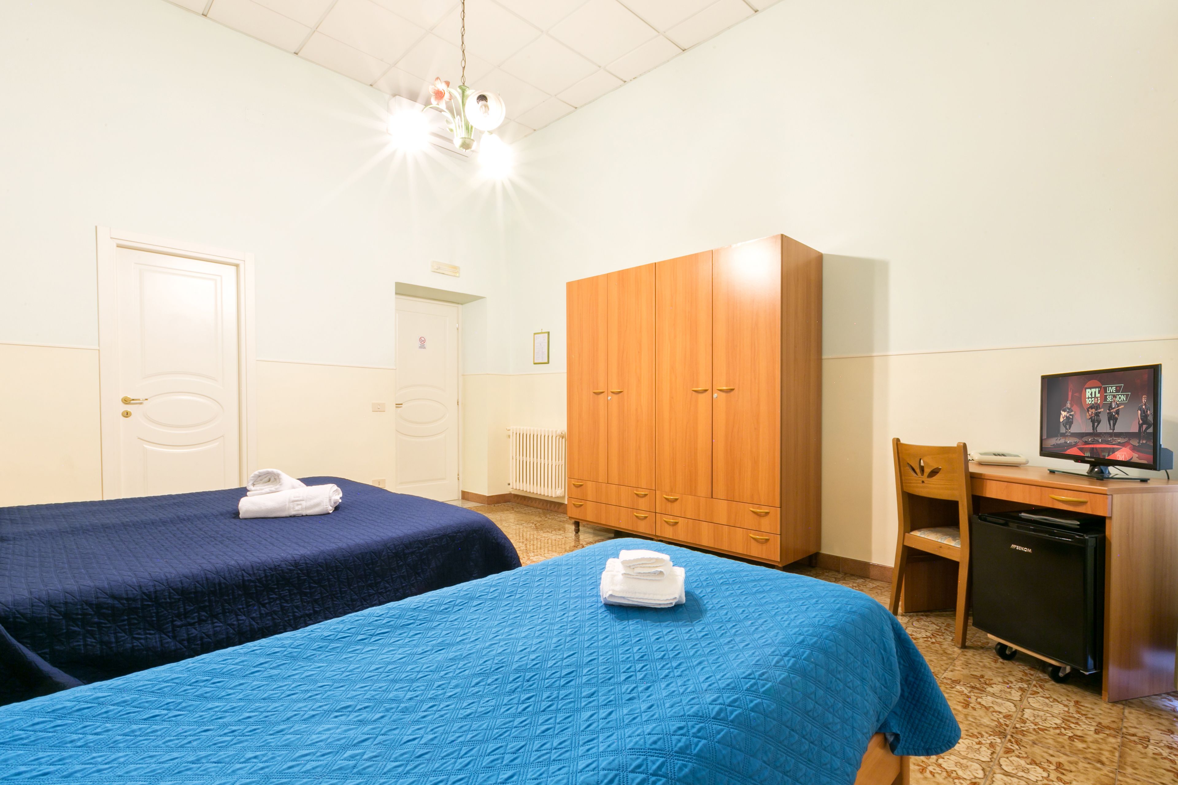 A room with two beds, a wardrobe, a desk with a computer, and a television.