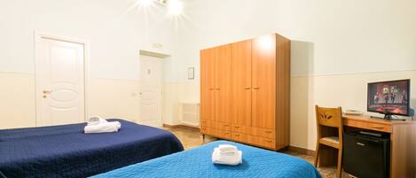 A room with two beds, a wardrobe, a desk with a computer, and a television.