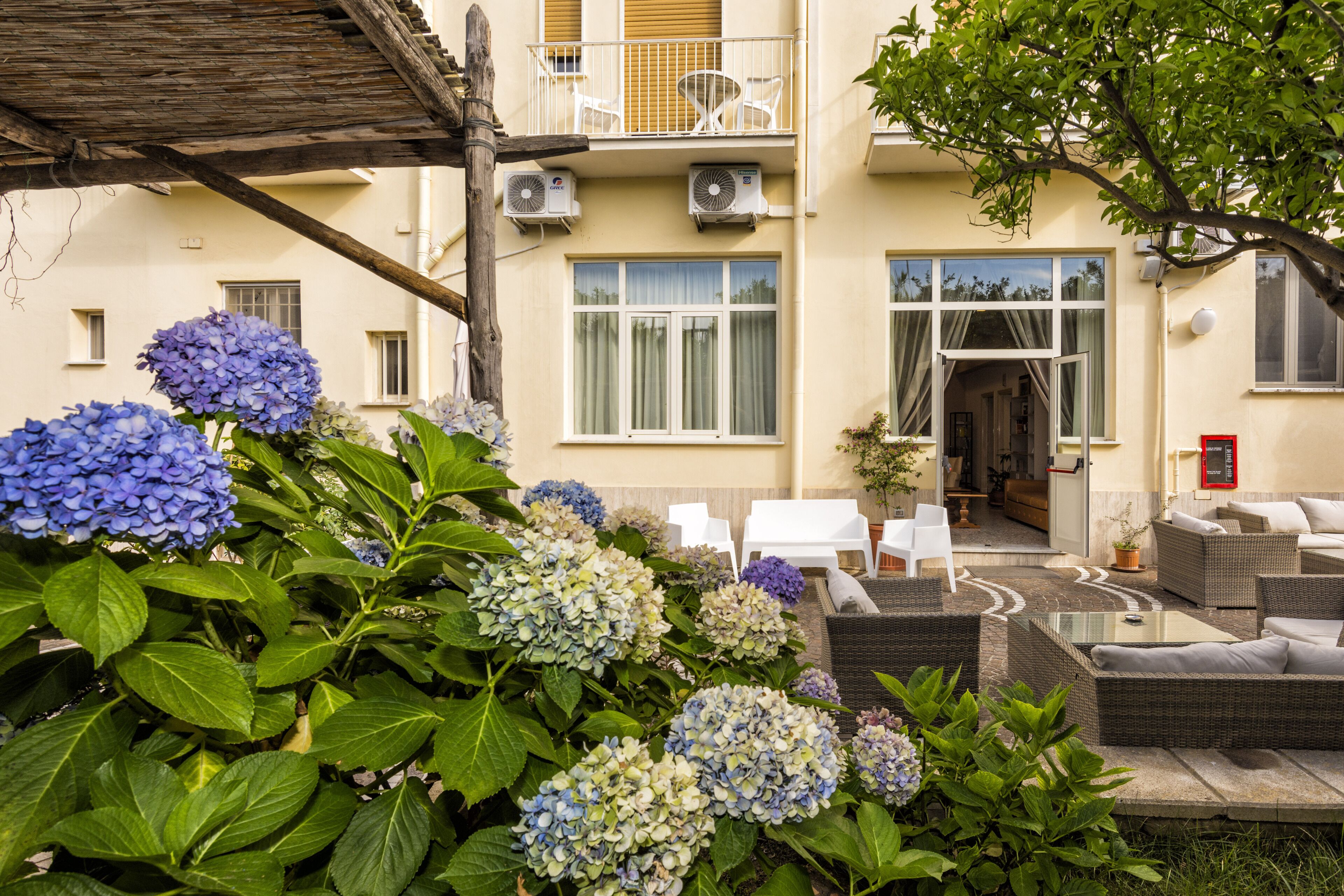 Een hotel met balkon, buitenmeubilair en een tuin vol hortensia's.