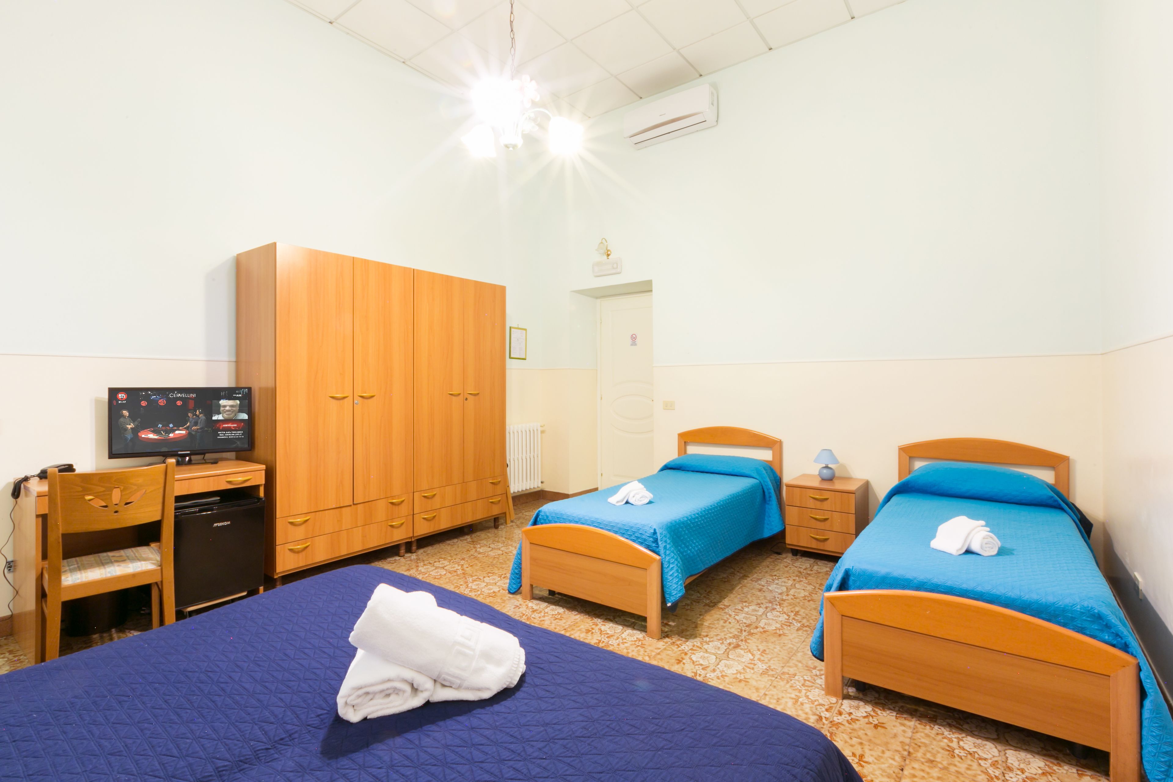 A hotel room with two beds, a desk with a computer, a wardrobe, and a television.