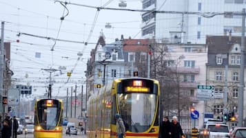 A tram station with two trams, overhead wires, and buildings in the background.